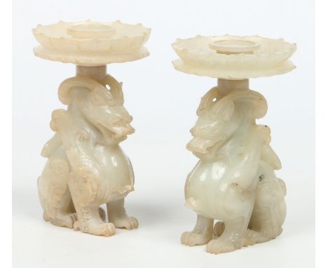A pair of Chinese carved opaque celadon jade candle stands of archaistic form. Each modelled as a seated mythical beast with 