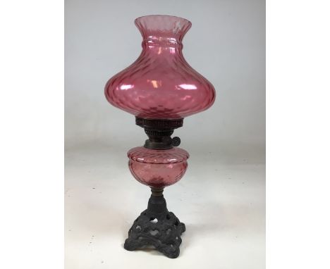 A vintage oil lamp with cranberry glass style shade - on decorative iron base. Some colour loss to glass also with a brass oi