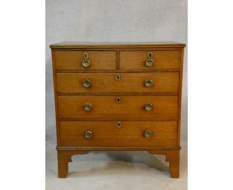 An early 19th century light oak chest of two short over three long drawers fitted with original brasswork on shaped bracket f