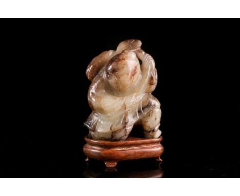 A Chinese carved cream/ khaki green jade figure of a boy with a large peach upon his back. With carved shaped hardwood stand.