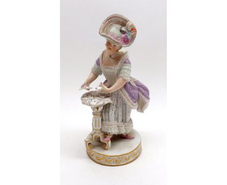 A Meissen Figure of Lady Card Player in 19th Century Costume, wearing a lilac coat and striped skirt, with suits of cards in 