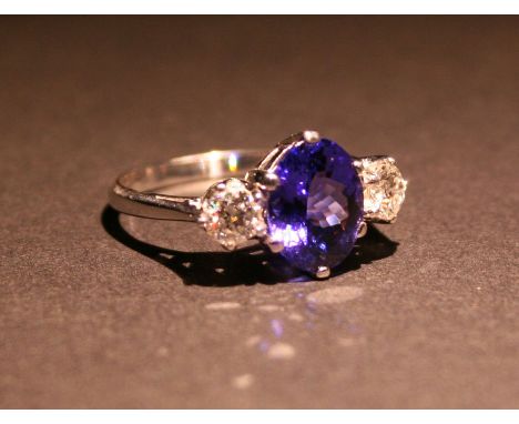 An 18ct. White Gold Tanzanite and Diamond Three Stone Ring with a central oval tanzanite flanked by diamonds within a pierced