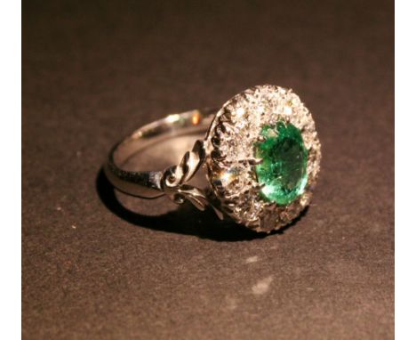 An 18ct. White Gold Emerald and Diamond Cluster Ring, set with a central oval emerald surrounded by diamonds within a pierced