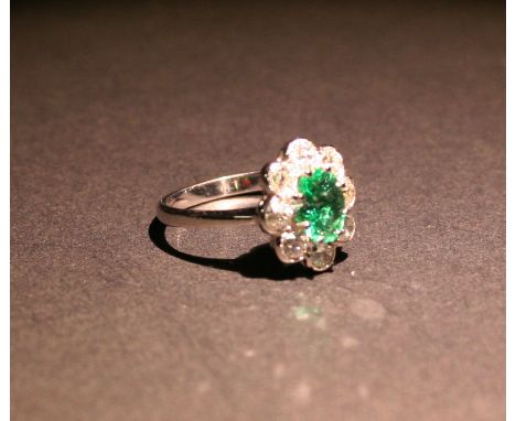 An 18ct. White Gold Emerald and Diamond Cluster Ring, with a central oval emerald surrounded by diamonds within a pierced set