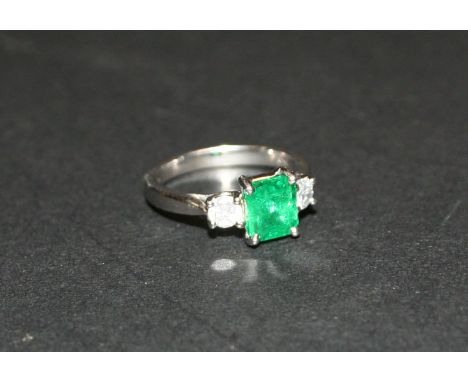 An 18ct. White Gold Emerald and Diamond Ring, with a central rectangular emerald flanked by diamonds, approximately 1.45/0.34