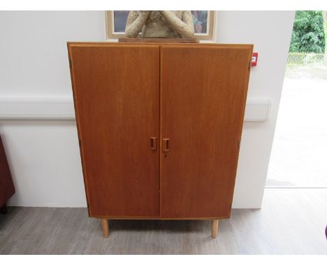 A Danish Borge Mogensen light oak twin door bookcase, shelved interior, raised on tapering legs. 100cm x 33cm x 136cm 