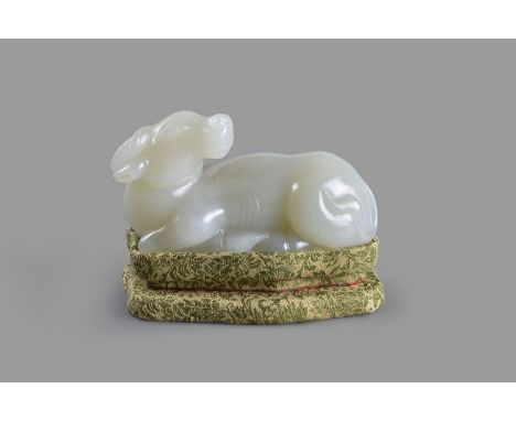 A Chinese pale celadon jade Bullock, 20th century, recumbent, with head turned back, 11.5cm long, on fabric covered shaped st