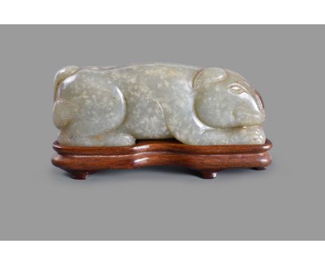 A Chinese mottled celadon jade model of a dog, Qing or earlier, the recumbent animal carved with its paws tucked under its bo