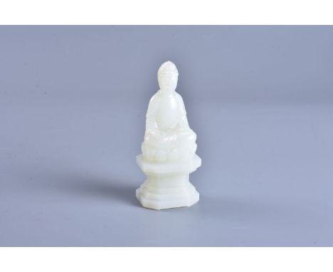 A white jade figure of buddha, seated in virasana on a raised lotus base with a serene facial expression, dressed in long ele