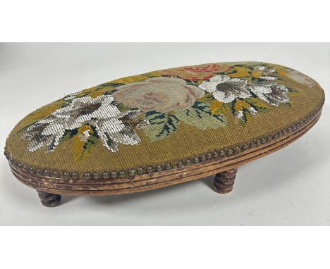 A Victorian treen oval foot rest with reeded moulded edge upholstered in beaded floral tapestry panel raised on ring turned s