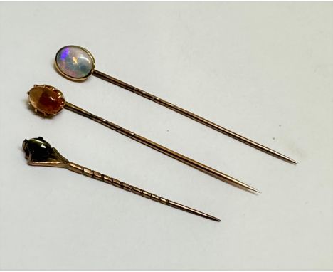 A yellow metal oval mounted water opal stick pin in rub over setting, (1cm x 0.6cm), a yellow metal stick pin set oval fire c