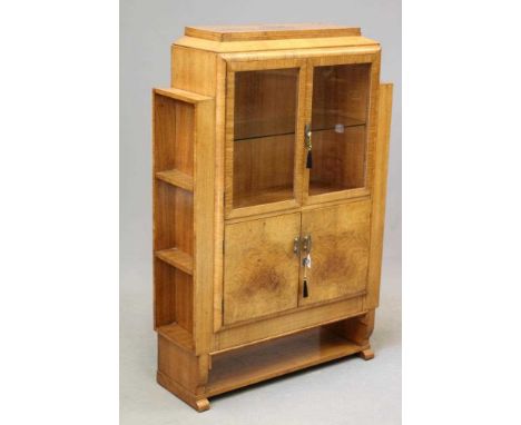 AN ART DECO WALNUT CABINET, the stepped oblong top over a pair of glazed cupboard doors above solid doors all enclosing shelv