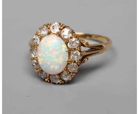 AN OPAL AND DIAMOND CLUSTER RING, the oval cabochon polished opal claw set to a border of twelve old cut diamonds to open scr
