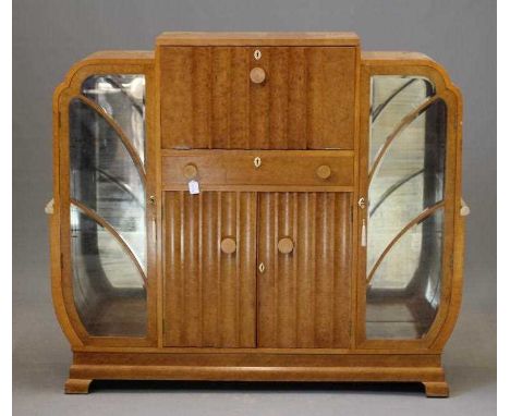 AN ART DECO BIRD'S EYE MAPLE COCKTAIL CABINET of stepped rounded oblong form, the centre hinged top and fluted fall opening t