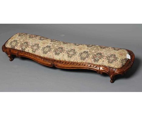 A VICTORIAN CARVED WALNUT FENDER STOOL of serpentine oblong form upholstered in a tapestry weave, scroll edged frame carved w