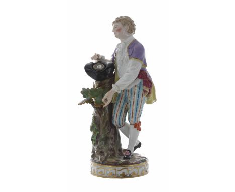 Meissen porcelain figure of a young man, standing by a tree trunk, with a small basket of eggs in his hat, with a blue crosse