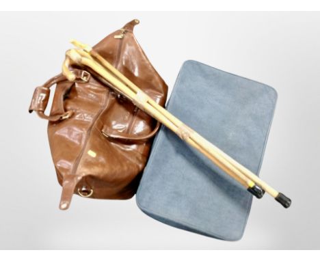 A vintage luggage case, a stitched brown leather hold all, and a bundle of four walking sticks.