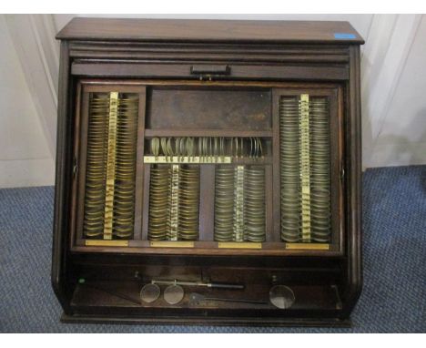 An early 20th century optician's oak cabinet with a tambour front, enclosing a removable tray with lenses over two drawers, a