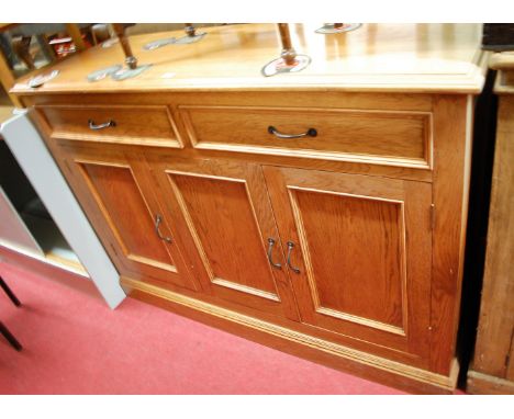 A contemporary light oak three door sideboard having twin frieze drawers and iron handles, width 143cm