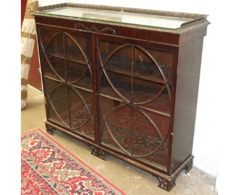 A 20th century mahogany floor-standing display cabinet with carved gallery top above a pair of astragal-glazed doors, (one da