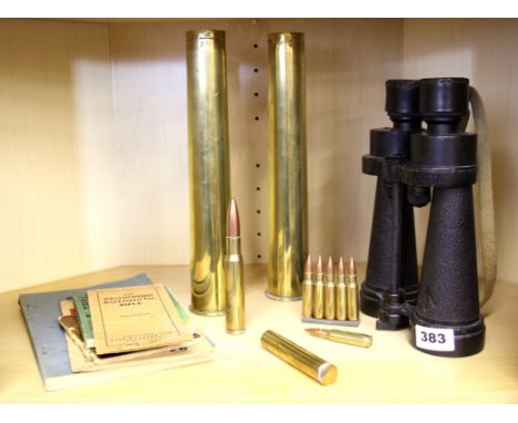 A pair of military binoculars, brass ammunition and related books.