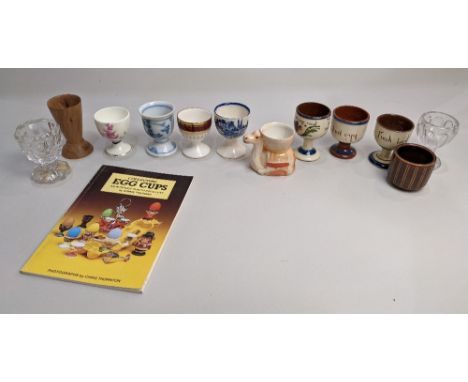 A small collection of egg cups in porcelain, glass and wood, to include a Wedgwood 'Pennine' egg cup, and a novelty camel sha