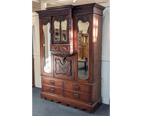 An Art Nouveau carved mahogany breakfront wardrobe central protruding cupboard with shaped mirrored doors and two small drawe