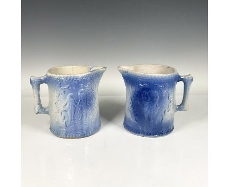 Two blue and white stoneware pitchers depicting a boy and girl between tree boughs. One pitcher has slightly darker coloring 
