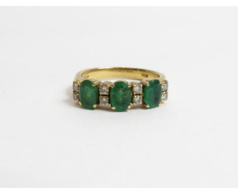 A diamond and emerald 18 carat gold half hoop ring, the three oval cut emeralds alternating with four pairs of brilliant cut 