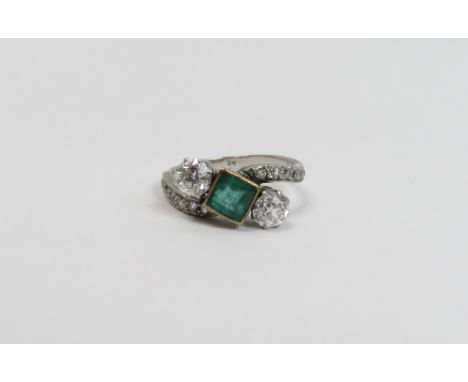 A diamond and emerald three stone cross over ring, in an unmarked white mount, the emerald measuring approximately 5.7mm by 5