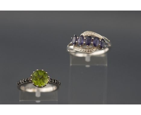 A white metal single stone peridot ring with gem set shoulders together with a white metal five stone amethyst ring. Both mar