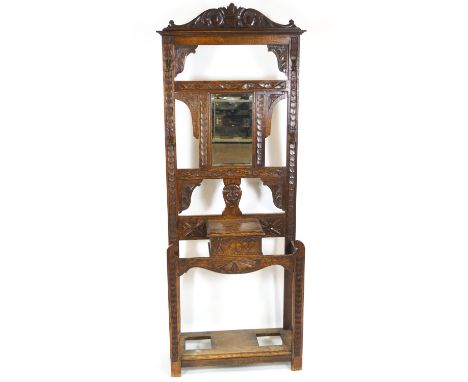 An oak hall stand with pierced top carved with grotesque and set a central glass over a glove box and two stick/umbrella stan