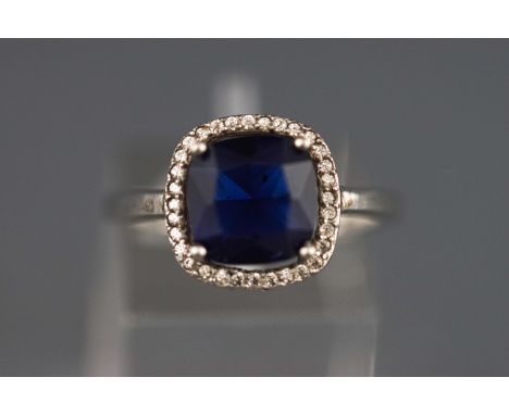 A white metal cluster ring set with a cushion cut synthetic sapphire and surrounded by cubic zirconia. Stamped 925 for Sterli