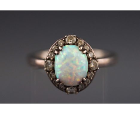 A white metal cluster ring set with synthetic opal cabochon and cubic zirconias. Stamped 925 for sterling silver. Size P 5.1 