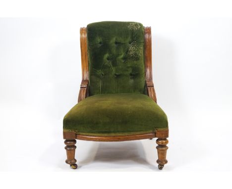An Edwardian mahogany button back armchair with carved curved side rails above an over stuffed seat raised on turned legs, 86