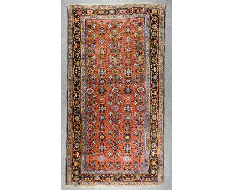 An Early 20th Century Malayer Carpet woven in colours the field filled with stylised floral motifs on a rose ground within th