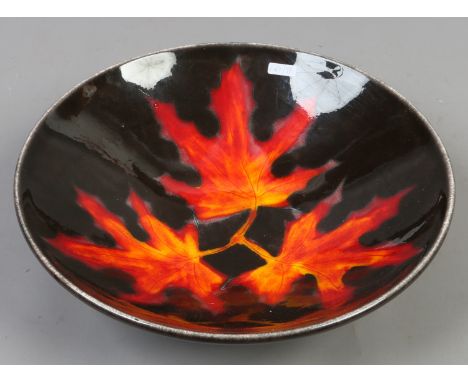 A Poole pottery bowl decorated with autumnal leaves on a black ground.