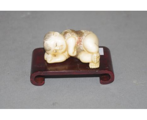 Antique Japanese ivory netsuke - sleeping child C1920's, on a timber stand, signed to base, width 4.5cm approx (netsuke only)