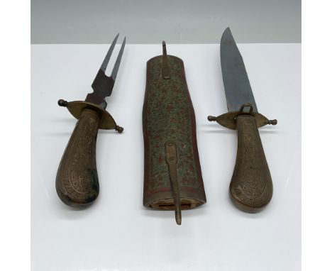 This antique knife and fork set features intricately engraved brass handles and a matching decorative brass scabbard with a f