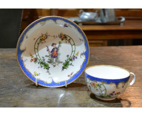 A Meissen cup and saucer painted in the French taste with figures within a green cartouche and with a scale blue and gilt bor