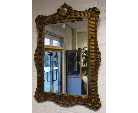 A reproduction gilt wall mirror, with ceramic plaque to top, 92cm high x 62cm wide