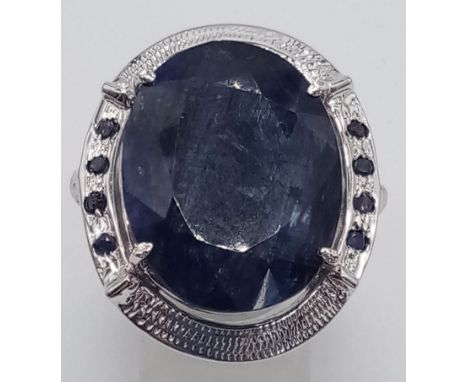 A sterling silver ring with a large oval cut blue sapphire surrounded by a silver halo with eight small blue sapphires. Ring 