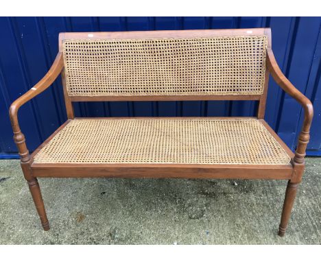 A 20th Century Indian teak framed bench with caned back and seat on turned and ringed tapering front legs, 122 cm wide x appr