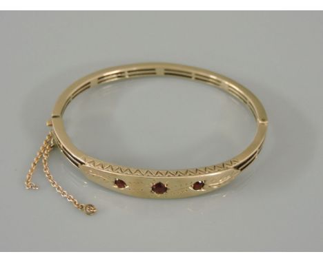 A gold hinged bangle, set with three garnets in star settings, tested as approximately 9ct gold, 15.6g