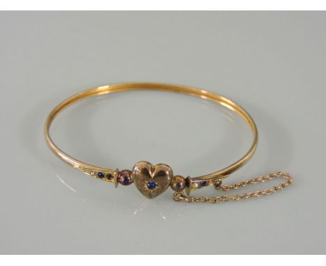 A gold sprung bangle, with heart centrepiece set with blue paste stones and split pearls, marked 9c, two pearls deficient, 4g