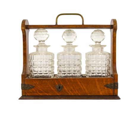 An early 20th century oak tantalus - with three clear glass decanters and brass fittings, 34cm wide.