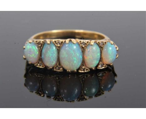 Late Victorian opal five stone ring with five graduated oval cabochon opals in carved scroll setting with diamond accents on 