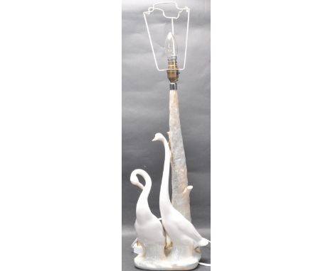 A Lladro Valencian ceramic lamp base in the form of two swans sitting at the base of a tree trunk with light fixture mounted 