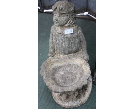 A SMALL WEATHERED CAST CONCRETE BIRD BATH in the form of a child by a hollowed trunk 