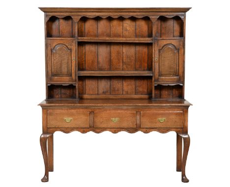 An oak dresser, early 19th c and later, the boarded rack with spice cupboards, the base with undulating apron, on cabriole le